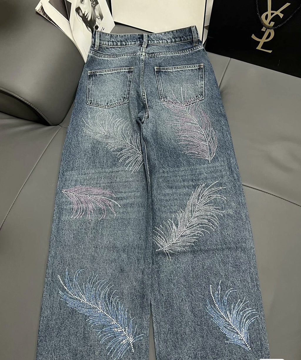 2026 Feather & Rhinestone Jeans: Featuring a high-waisted, wide-leg silhouette crafted from blue denim, with a unique feather and rhinestone embellishment design.