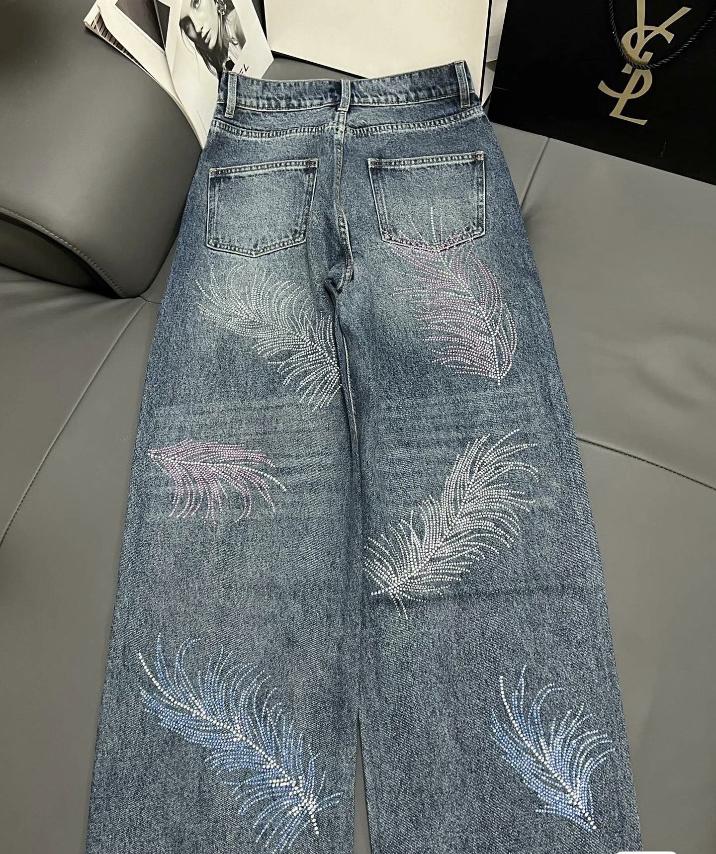 2026 Feather & Rhinestone Jeans: Featuring a high-waisted, wide-leg silhouette crafted from blue denim, with a unique feather and rhinestone embellishment design.